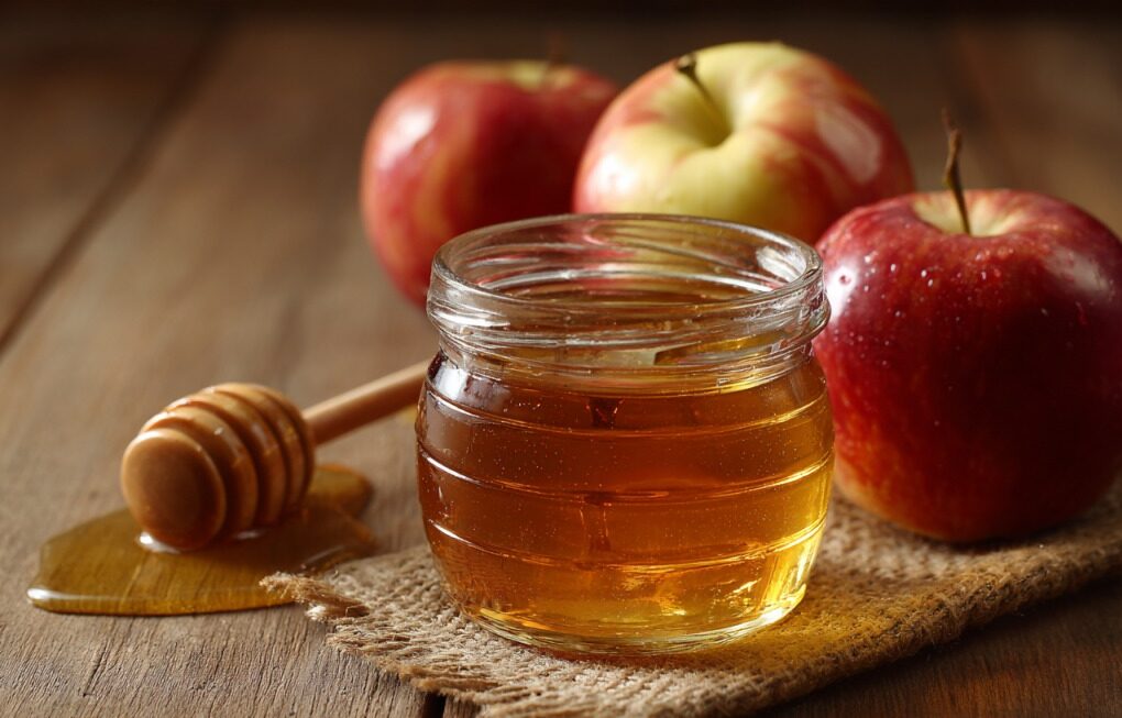 Tegla meda sa drvenom kašikom i svežim jabukama na stolu