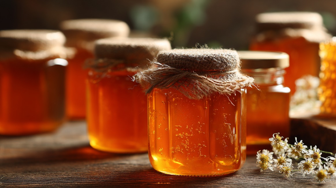 Staklene tegle sa zlatnim medom na drvenoj površini u toplom svetlu