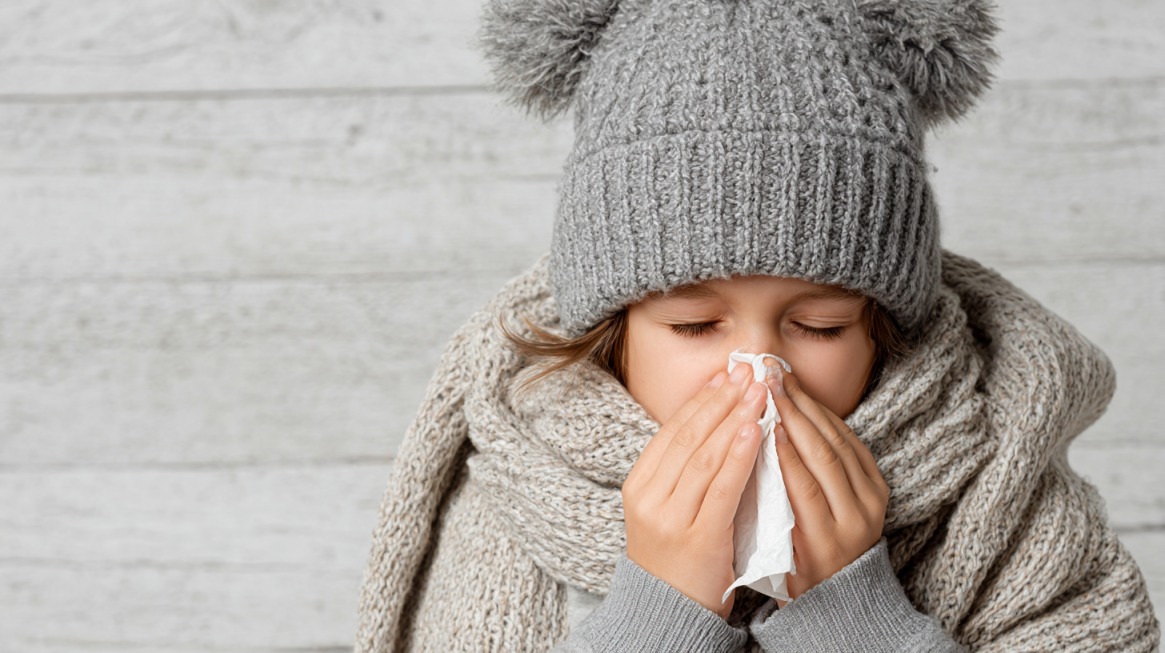 Dete u vunenoj kapi i šalu duva nos u maramicu